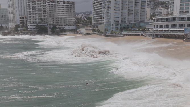 Two of the three swimmers can barely be seen in the large waves.